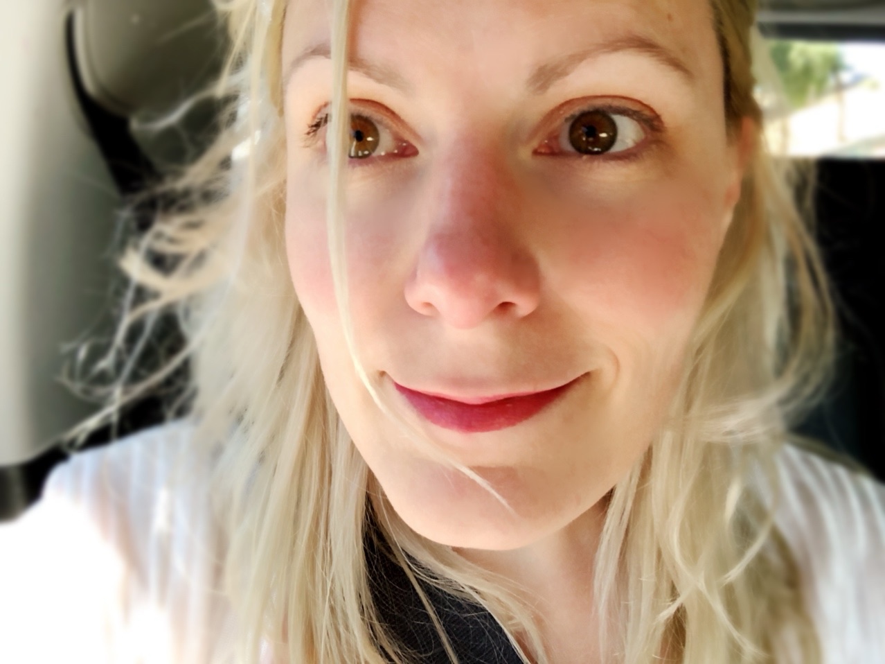 A selfie of Scout, sitting in the back seat of a car, with a smile on her face, the window rolled down, and her blonde hair blowing in the wind.